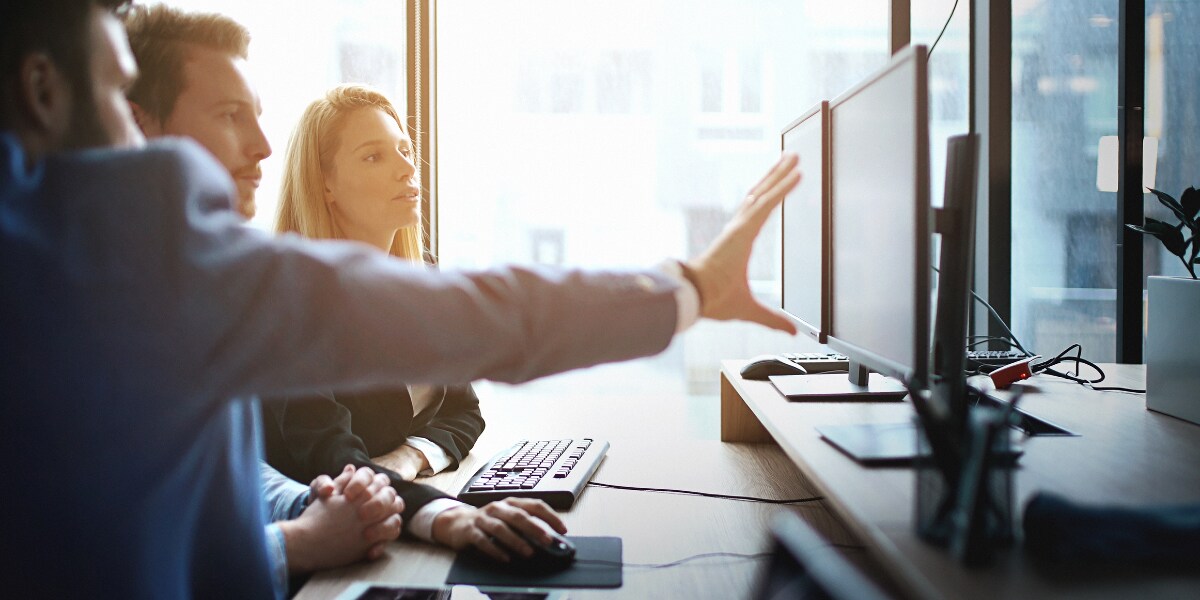 three people sitting at desk looking at monitor