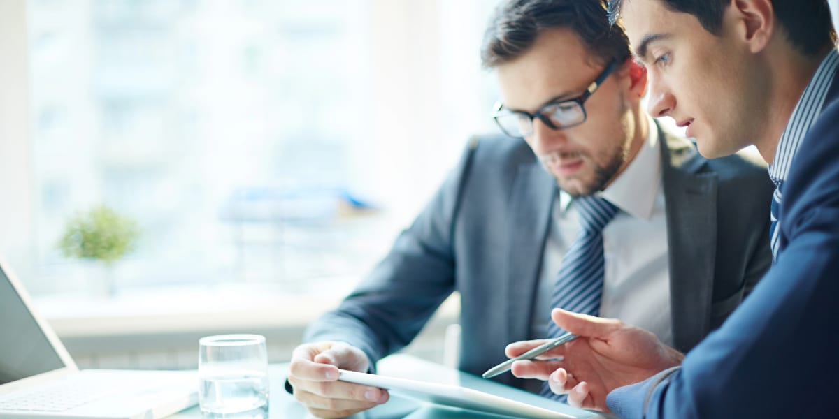 two people wearing suits looking at tablet screen